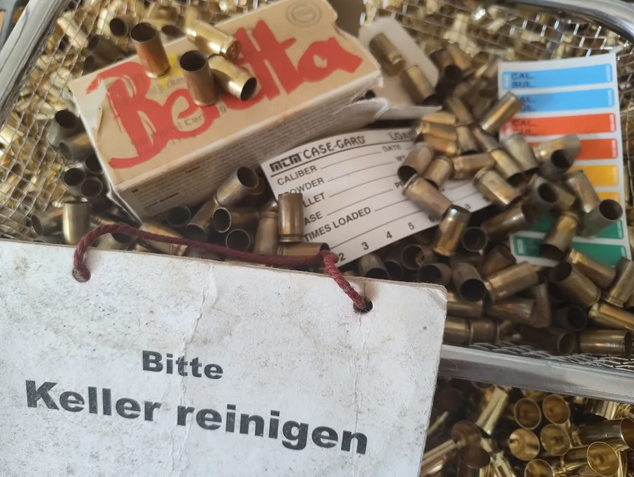 Abgenutzte und mehrfach beschriftete Pappschachtel zwischen unsortierten Patronenhülsen